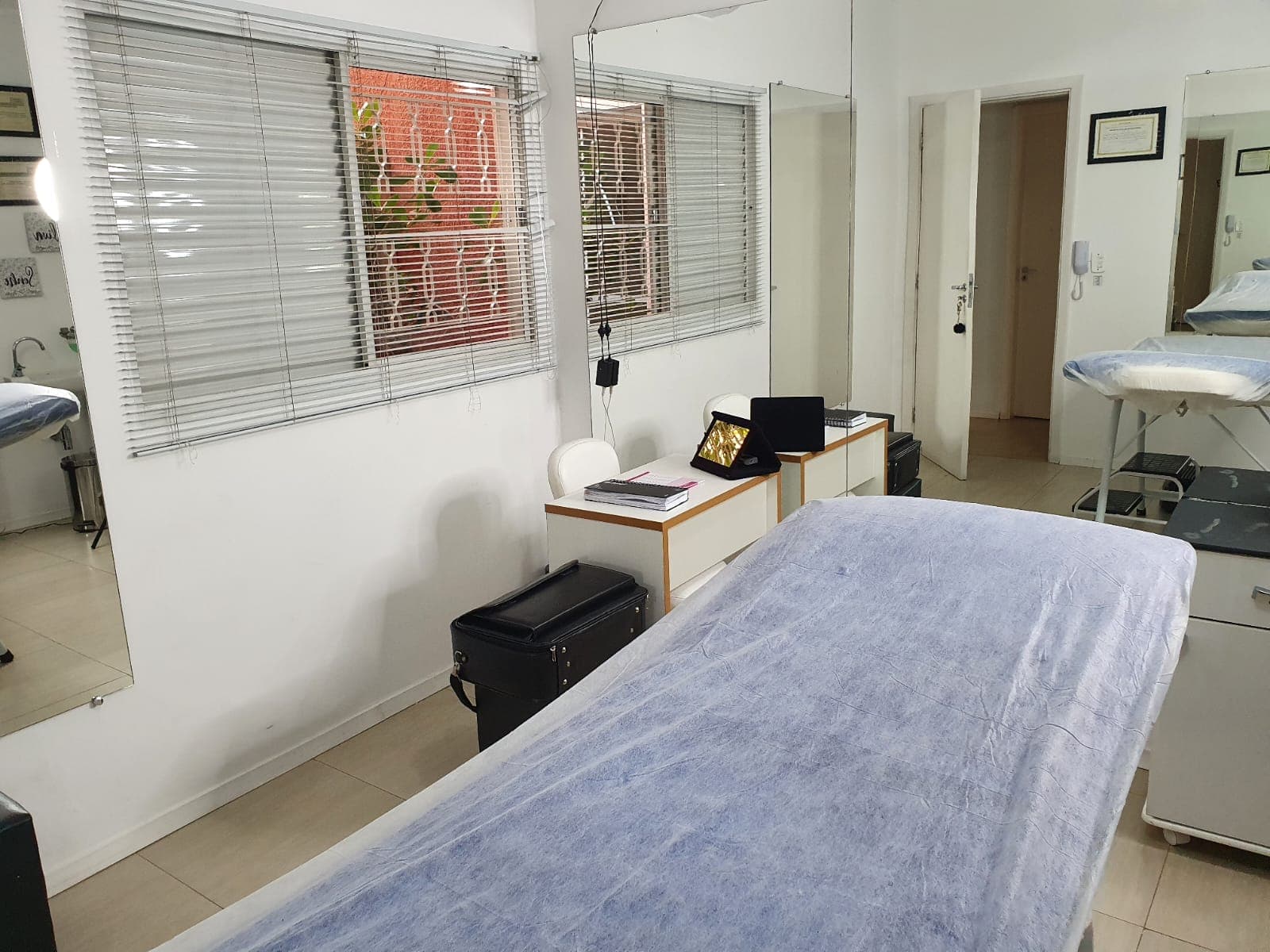 Sala de atendimento com maca, persianas e espelhos