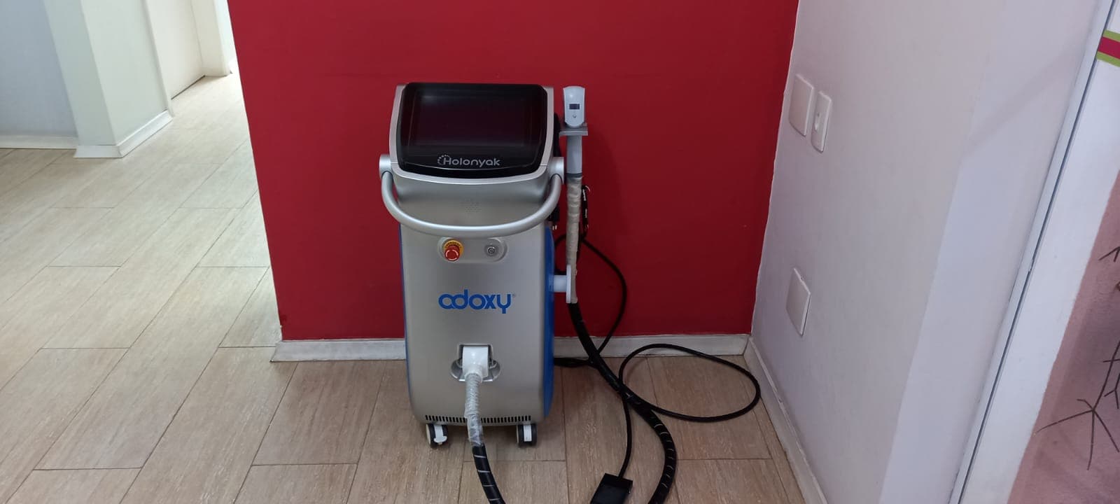 Aparelho Holonyak da Adoxy na frente da parede vermelha do consultório